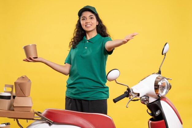 Vista frontal de mensajería femenina en uniforme verde con postre sobre fondo amarillo trabajo trabajo entrega mujer servicio trabajador comida sonrisa