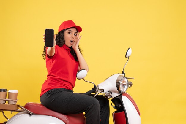 Vista frontal mensajero femenino en bicicleta para entrega de café sosteniendo el teléfono sobre fondo amarillo servicio de entrega uniforme trabajo trabajador mujer de trabajo