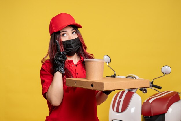 Vista frontal del mensajero femenino en máscara con comida de entrega en pared amarilla