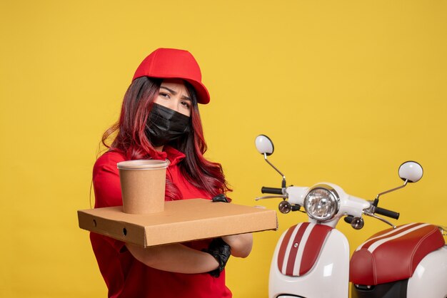 Vista frontal del mensajero femenino en máscara con comida de entrega en pared amarilla