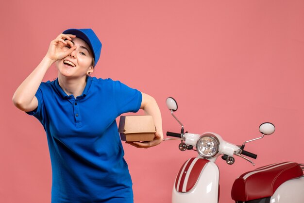 Vista frontal mensajero femenino con pequeño paquete de comida sonriendo en rosa trabajo servicio uniforme de entrega de trabajo bicicleta trabajador pizza mujer