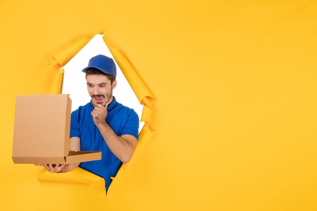 Vista frontal mensajero masculino abriendo la caja de pizza en el espacio amarillo