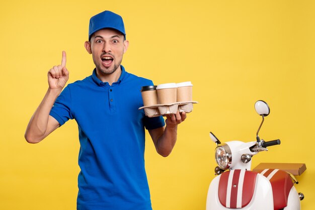 Vista frontal mensajero masculino con entrega de café en amarillo trabajo servicio de color uniforme de trabajo trabajador de bicicleta