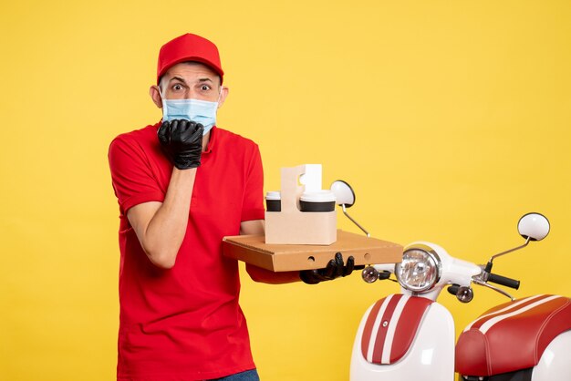 Vista frontal mensajero masculino con entrega de café y caja asustada en amarillo servicio de trabajo covid- virus pandemia uniforme de bicicleta de color