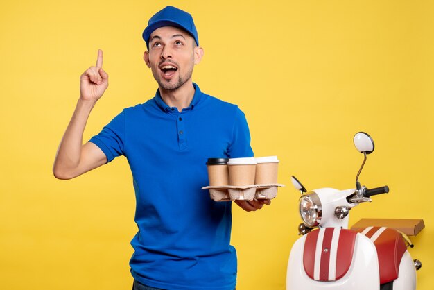 Vista frontal mensajero masculino con entrega de café en color amarillo servicio de trabajador trabajo emoción uniforme bicicleta