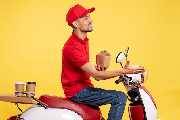 Vista frontal mensajero masculino joven en uniforme rojo con poca comida de entrega sobre fondo amarillo