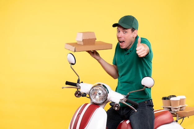 Vista frontal mensajero masculino joven en uniforme sosteniendo paquetes de alimentos en amarillo