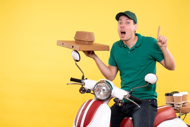 Vista frontal mensajero masculino joven en uniforme sosteniendo paquetes de alimentos en amarillo