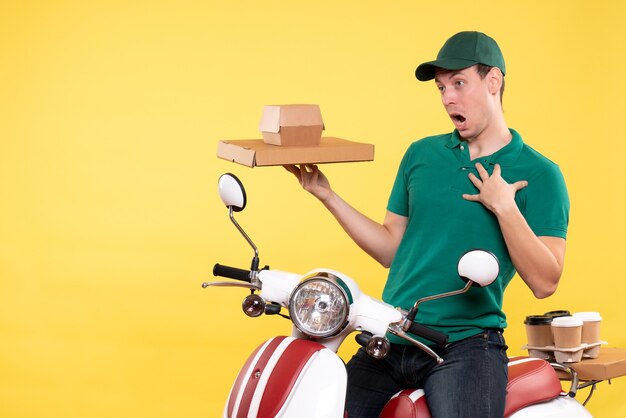 Vista frontal mensajero masculino joven en uniforme sosteniendo paquetes de alimentos en amarillo