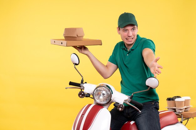 Vista frontal mensajero masculino joven en uniforme sosteniendo paquetes de alimentos en amarillo