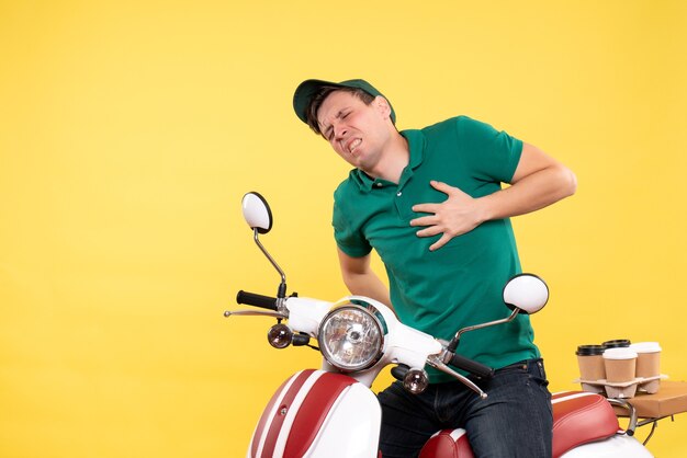 Vista frontal mensajero masculino joven en uniforme verde en bicicleta con dolor de corazón amarillo