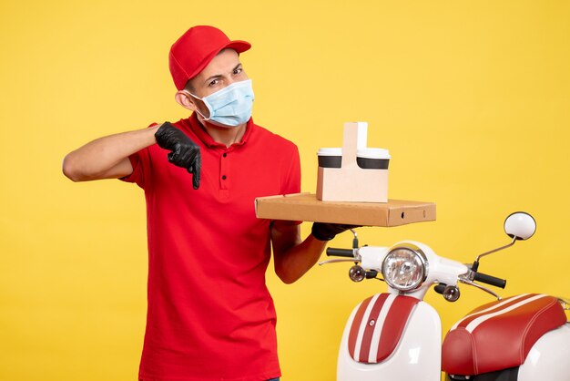 Vista frontal mensajero masculino en máscara con entrega de café y caja en colores amarillos servicio covid- trabajo uniforme de trabajo de virus pandemia