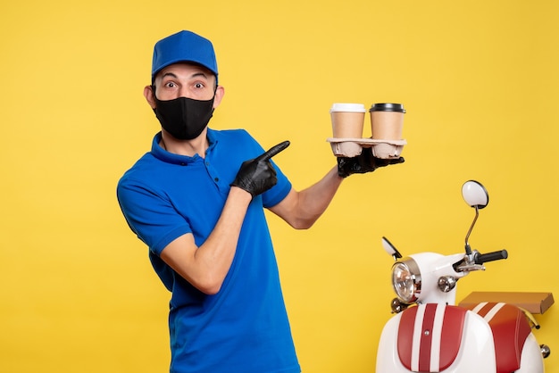 Vista frontal mensajero masculino en máscara negra sosteniendo café en un trabajo amarillo covid- servicio de trabajo uniforme de entrega pandémica