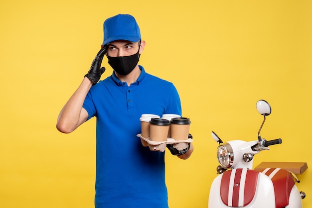 Foto gratuita vista frontal mensajero masculino en máscara negra sosteniendo café en un trabajo amarillo covid- trabajo uniforme de entrega de servicios pandémicos