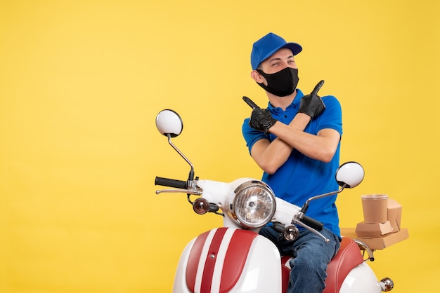 Vista frontal mensajero masculino sentado en bicicleta con máscara en servicio amarillo entrega pandémica covid- trabajo uniforme de trabajo