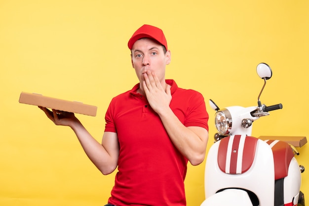 Vista frontal mensajero masculino sosteniendo una caja de pizza en color amarillo uniforme de trabajo de entrega de trabajo trabajador de bicicleta