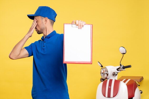Vista frontal mensajero masculino sosteniendo nota de archivo en uniforme de emoción de trabajo de bicicleta de servicio de trabajador de color amarillo