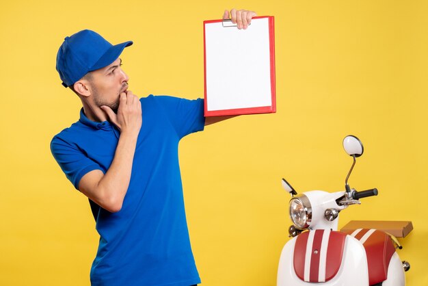 Vista frontal mensajero masculino sosteniendo nota de archivo en uniforme de emoción de trabajo de bicicleta de servicio de trabajador de color amarillo