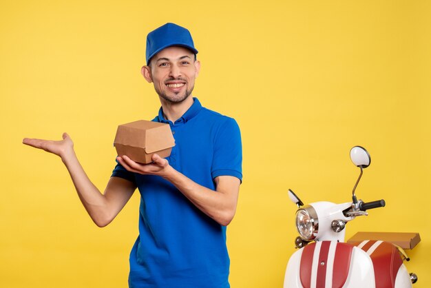 Vista frontal mensajero masculino sosteniendo un pequeño paquete de comida en amarillo trabajo colores servicio trabajo entrega uniforme trabajador en bicicleta