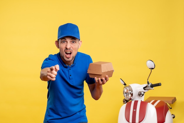 Vista frontal mensajero masculino sosteniendo un pequeño paquete de comida en amarillo trabajo colores servicio trabajo entrega uniforme trabajador