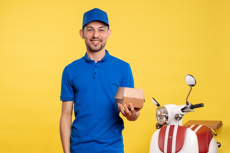Foto gratuito vista frontal mensajero masculino sosteniendo un pequeño paquete de comida en amarillo trabajo colores servicio uniforme trabajo en bicicleta trabajador de reparto