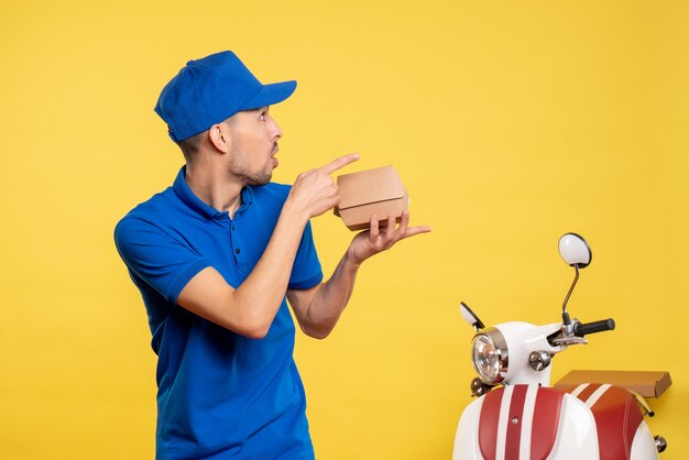 Foto gratuita vista frontal mensajero masculino sosteniendo un pequeño paquete de comida en amarillo trabajo colores servicio uniforme de trabajo trabajador en bicicleta