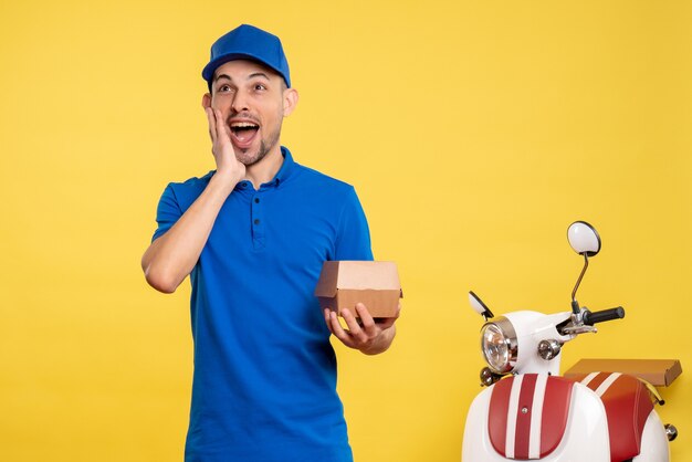 Vista frontal mensajero masculino sosteniendo un pequeño paquete de comida en color amarillo trabajador de entrega de trabajo en bicicleta de servicio de trabajo