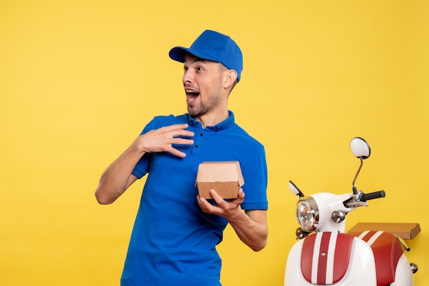 Vista frontal mensajero masculino sosteniendo un pequeño paquete de comida en el color amarillo del trabajador de entrega de trabajo en bicicleta uniforme de servicio de trabajo amarillo