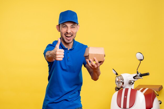 Vista frontal mensajero masculino sosteniendo un pequeño paquete de comida en el color amarillo del trabajador de entrega de trabajo en bicicleta uniforme de servicio de trabajo amarillo