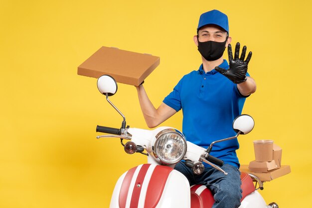 Foto gratuita vista frontal mensajero masculino en uniforme azul con caja de comida en amarillo virus pandemia covid entrega trabajo servicio trabajo bicicleta