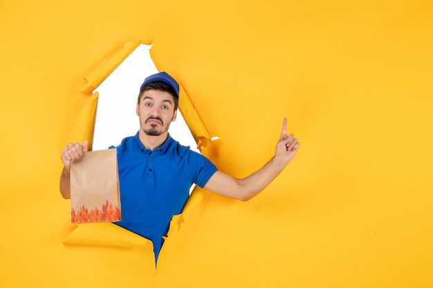 Vista frontal mensajero masculino en uniforme azul con paquete de alimentos en el piso amarillo trabajo de entrega de trabajo de servicio de trabajo de color de la foto del trabajador