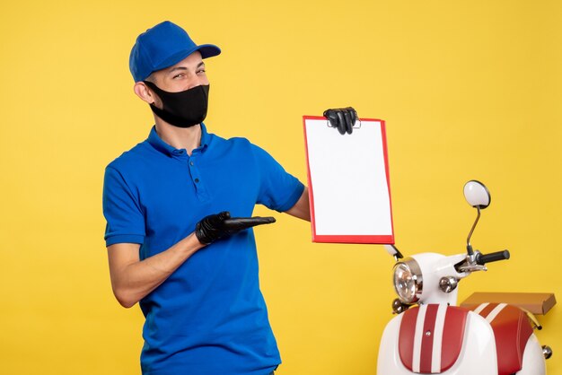 Vista frontal mensajero masculino en uniforme azul sosteniendo la nota de archivo en amarillo servicio de trabajo covid- trabajo uniforme de color de entrega