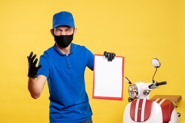 Vista frontal mensajero masculino en uniforme azul sosteniendo la nota de archivo en el servicio de trabajo amarillo covid- color pandémico de entrega de trabajo