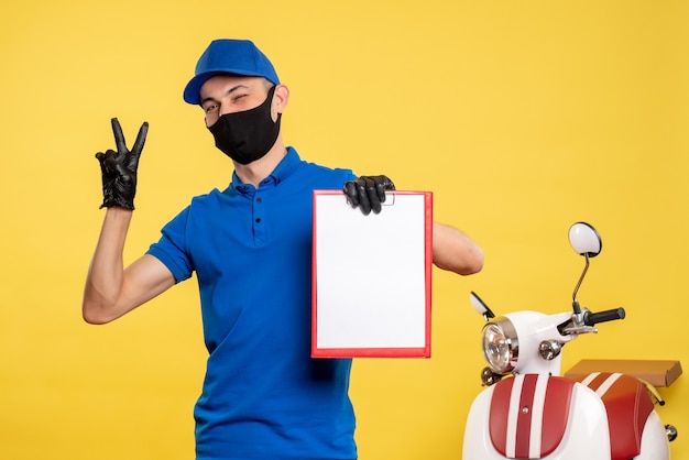 Vista frontal mensajero masculino en uniforme azul sosteniendo la nota de archivo en el servicio de trabajo amarillo covid- trabajo uniforme de color pandémico