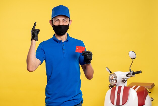 Vista frontal mensajero masculino en uniforme azul con tarjeta bancaria en amarillo servicio de trabajo covid- uniforme de color pandemia de entrega de trabajo