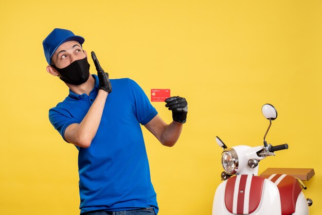 Vista frontal mensajero masculino en uniforme azul con tarjeta bancaria en un uniforme de servicio de trabajo amarillo covid- color pandémico de entrega de trabajo