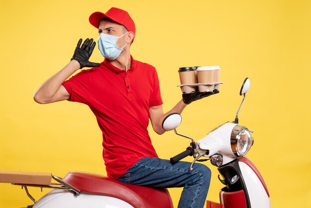 Vista frontal mensajero masculino en uniforme y máscara con café en el trabajo de color amarillo pandemia covid- virus de servicio de alimentos de trabajo