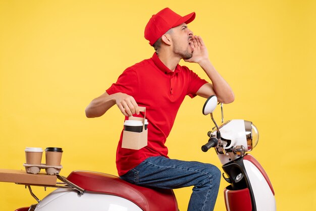 Vista frontal mensajero masculino en uniforme rojo con café en uniforme de color amarillo servicio de trabajo en bicicleta trabajador de entrega de trabajo