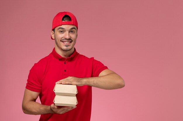 Vista frontal del mensajero masculino en uniforme rojo y gorra sosteniendo un pequeño paquete de entrega