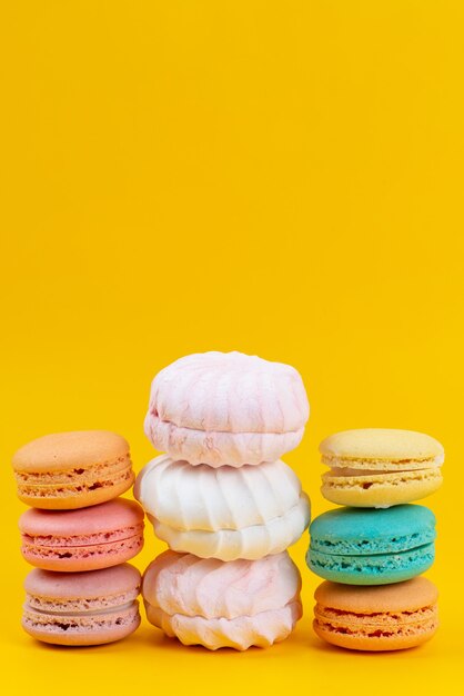 Una vista frontal de merengues y macarons deliciosos y aislados en amarillo, confitura dulce de galleta de pastel