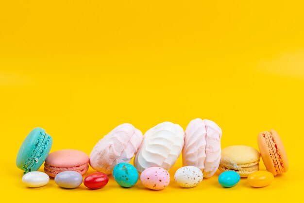 Una vista frontal de merengues y macarons deliciosos y dulces en amarillo, caramelo de arco iris de colores