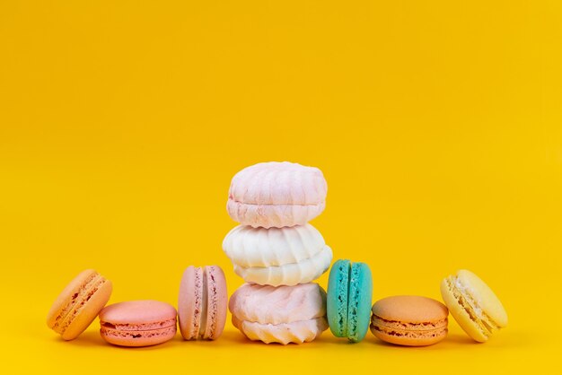 Una vista frontal de merengues y macarons deliciosos horneados en amarillo, pastel de color dulce de galleta