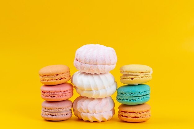 Una vista frontal de merengues y macarons deliciosos y pasteles horneados aislados en amarillo, confitura de galleta de pastel