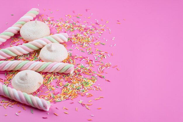 Una vista frontal de merengues y malvaviscos deliciosos con caramelos de colores en galleta de galleta de color rosa