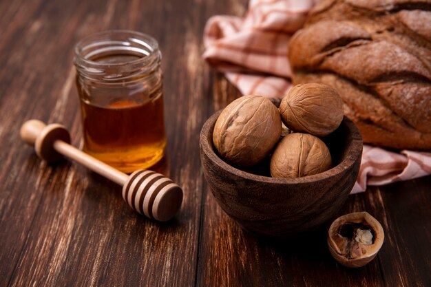 Vista frontal de la miel en un tarro con nueces y una hogaza de pan negro sobre un fondo de madera