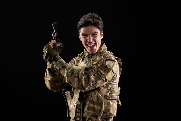 Vista frontal del militar emocional en uniforme con pistola en pared negra