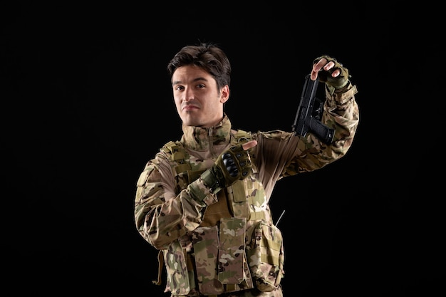 Vista frontal del militar en uniforme con pistola negra pared negra