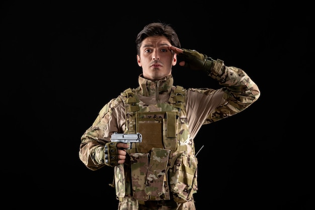 Vista frontal militar en uniforme con pistola en pared negra