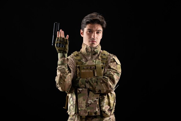 Vista frontal del militar en uniforme con pistola en pared negra