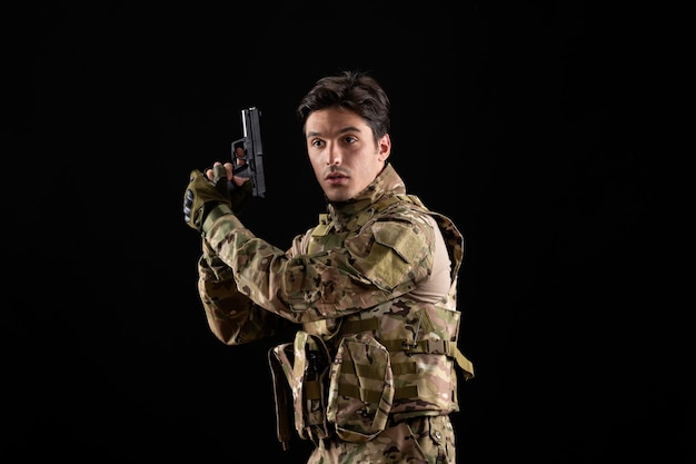 Foto gratuita vista frontal del militar en uniforme con pistola en pared negra